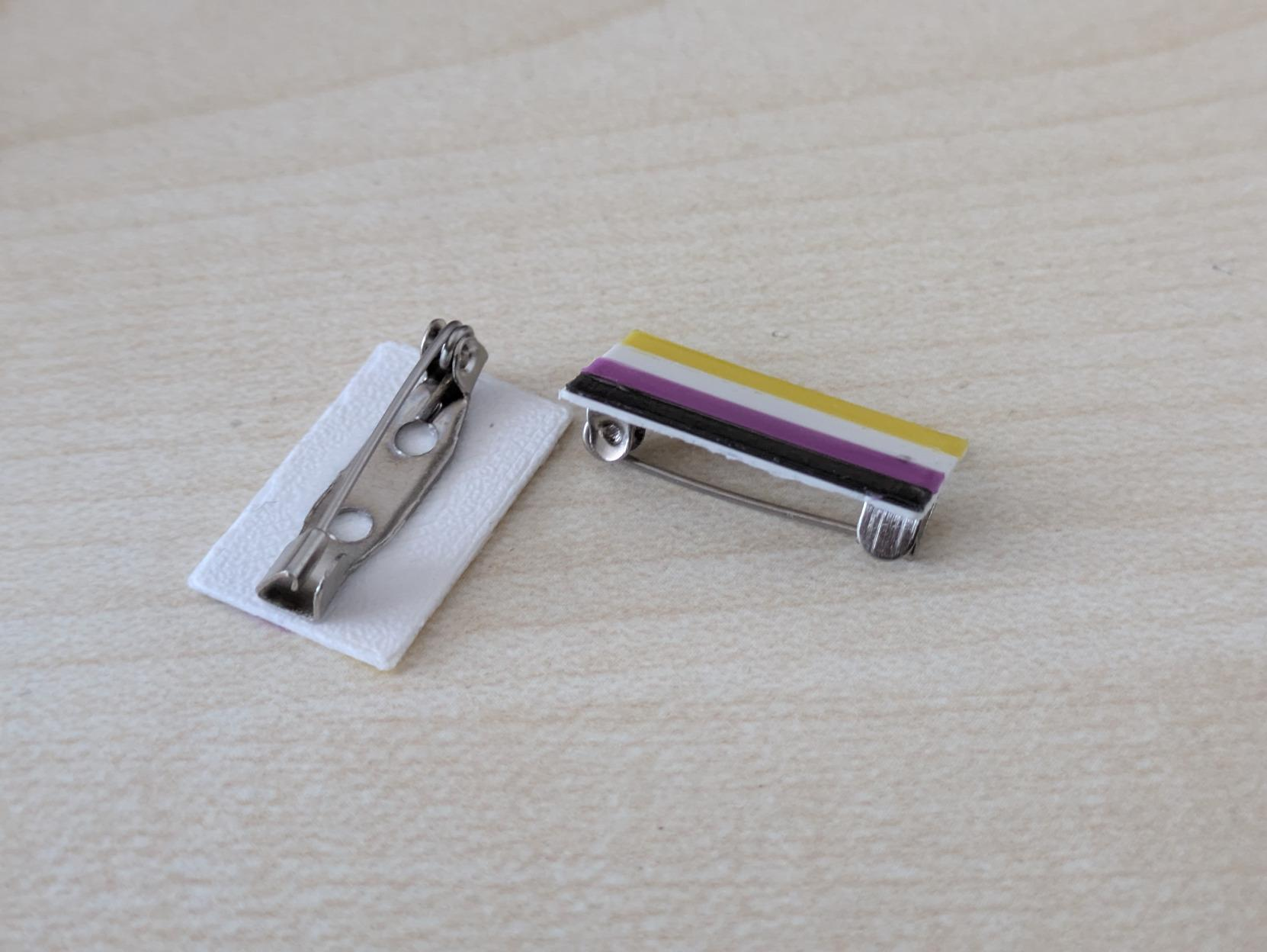 two pins with a nonbinary flag secured by a safety pin
